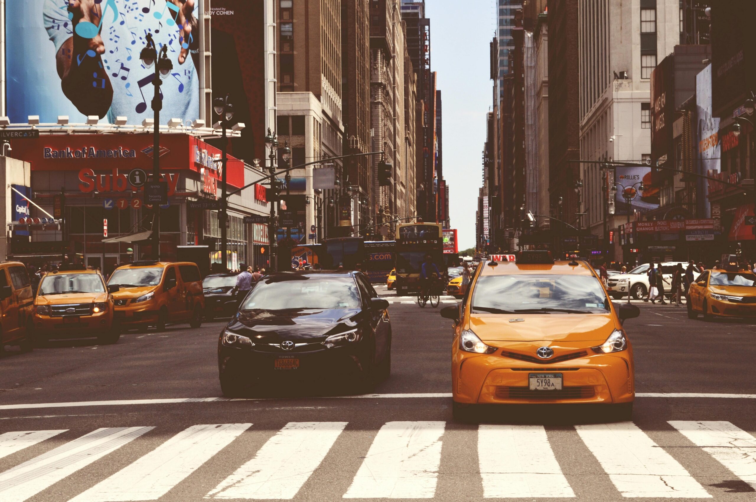 Dynamic street scene with taxis, cars, and pedestrians in a busy city intersection.