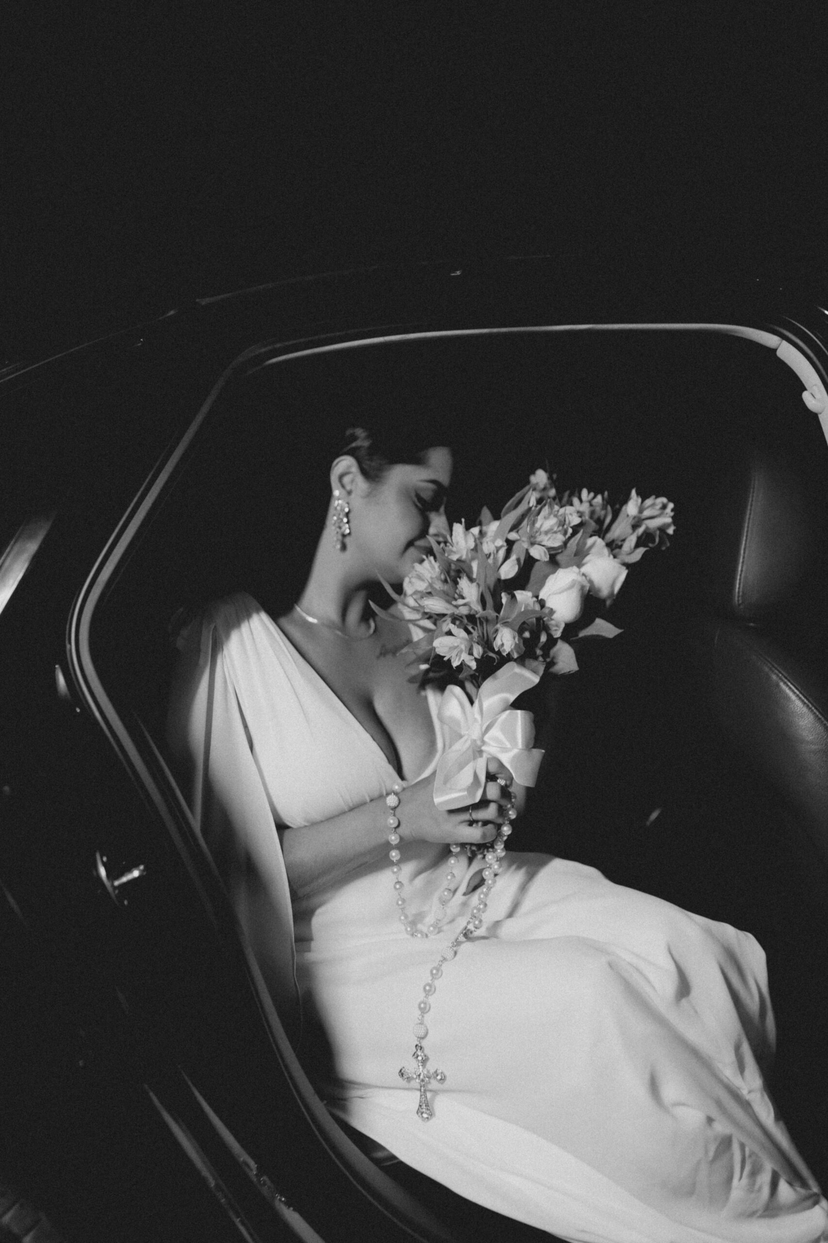 Stylish black and white photo of a bride with bouquet inside a luxury car.