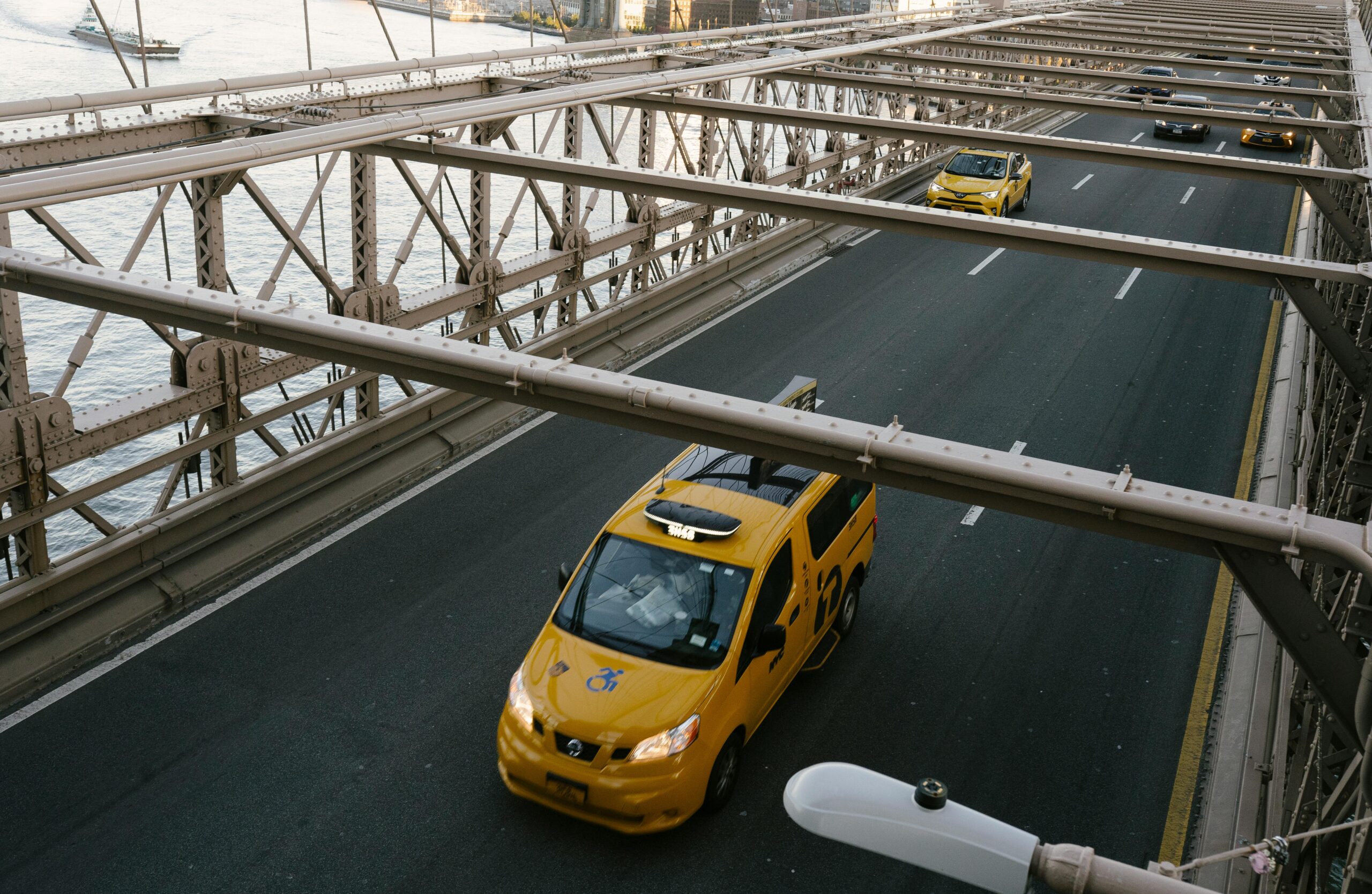 Yellow taxis driving across the Brooklyn Bridge with river views.